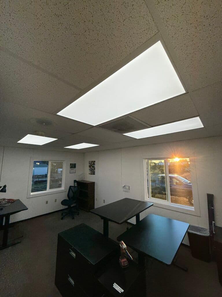 Bright office interior with fluorescent lighting, large windows, and black desks.