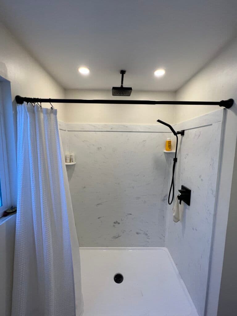 Modern shower with white marble walls, rainfall showerhead, and curtain. Bright, inviting space.