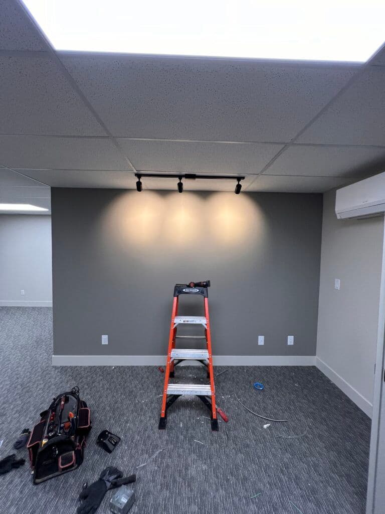 Interior room with gray wall, spotlight lighting, orange ladder, and tools on the floor.