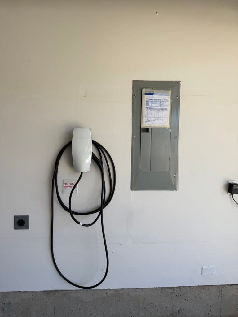 Electric vehicle charging station mounted on garage wall with power panel nearby.
