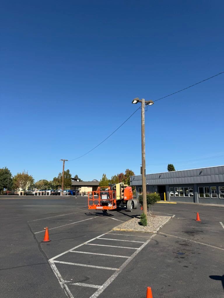 Scene of an orange lift truck parked in a vacant lot under a clear blue sky.
