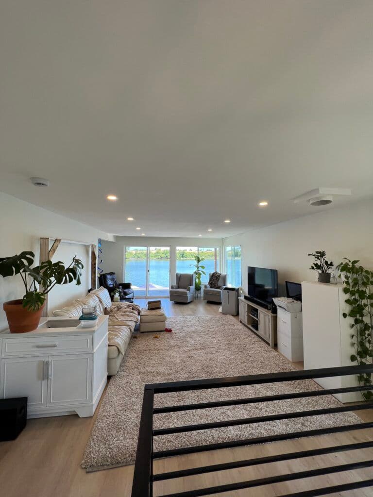 Spacious modern living room with large windows, white furniture, and natural light.