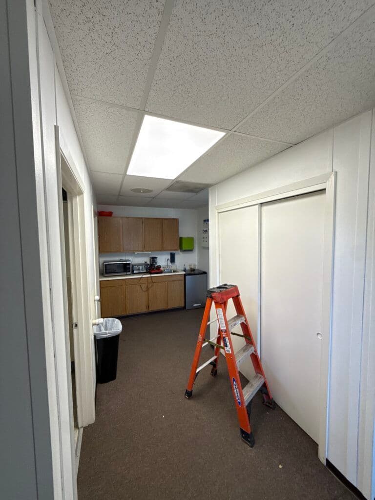 Interior hallway with a kitchen area, ladder, and storage closet. Bright overhead lighting.
