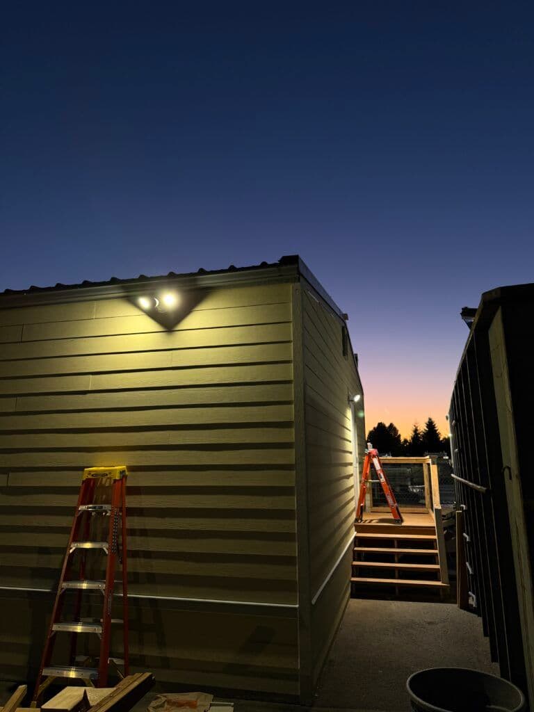 Exterior view of a building at dusk, showcasing lights and a ladder by the entrance.