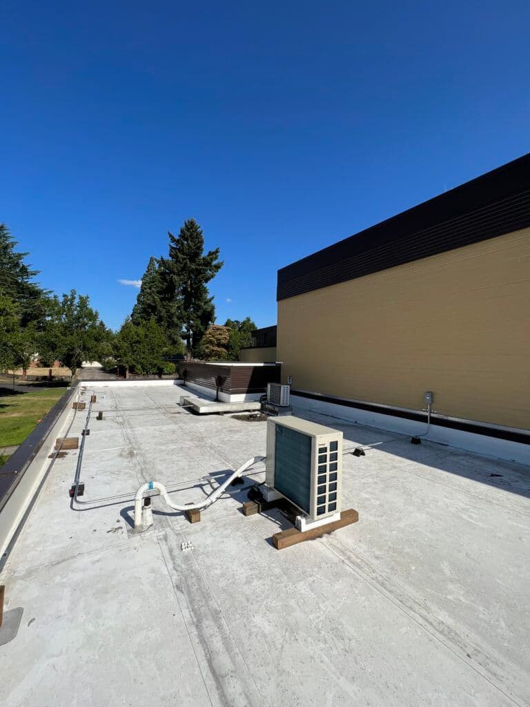 Roof with HVAC unit, clear blue sky and green trees in the background, focusing on infrastructure.